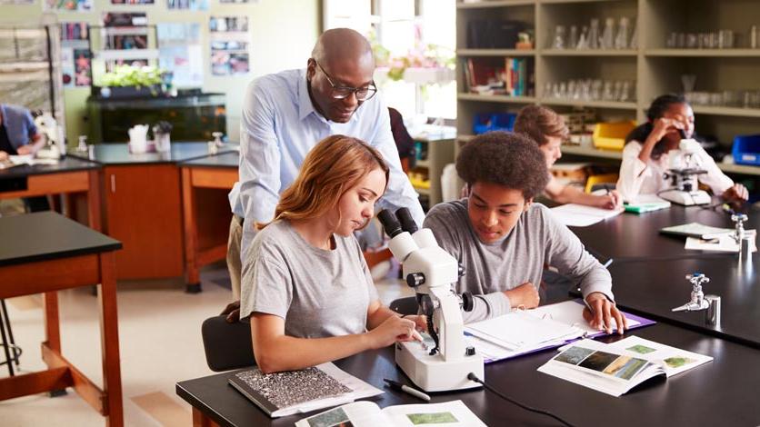 Teacher observes high school students using microscope in biology class