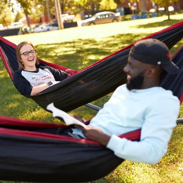 Two students laughing while studying in hammocks on lawn